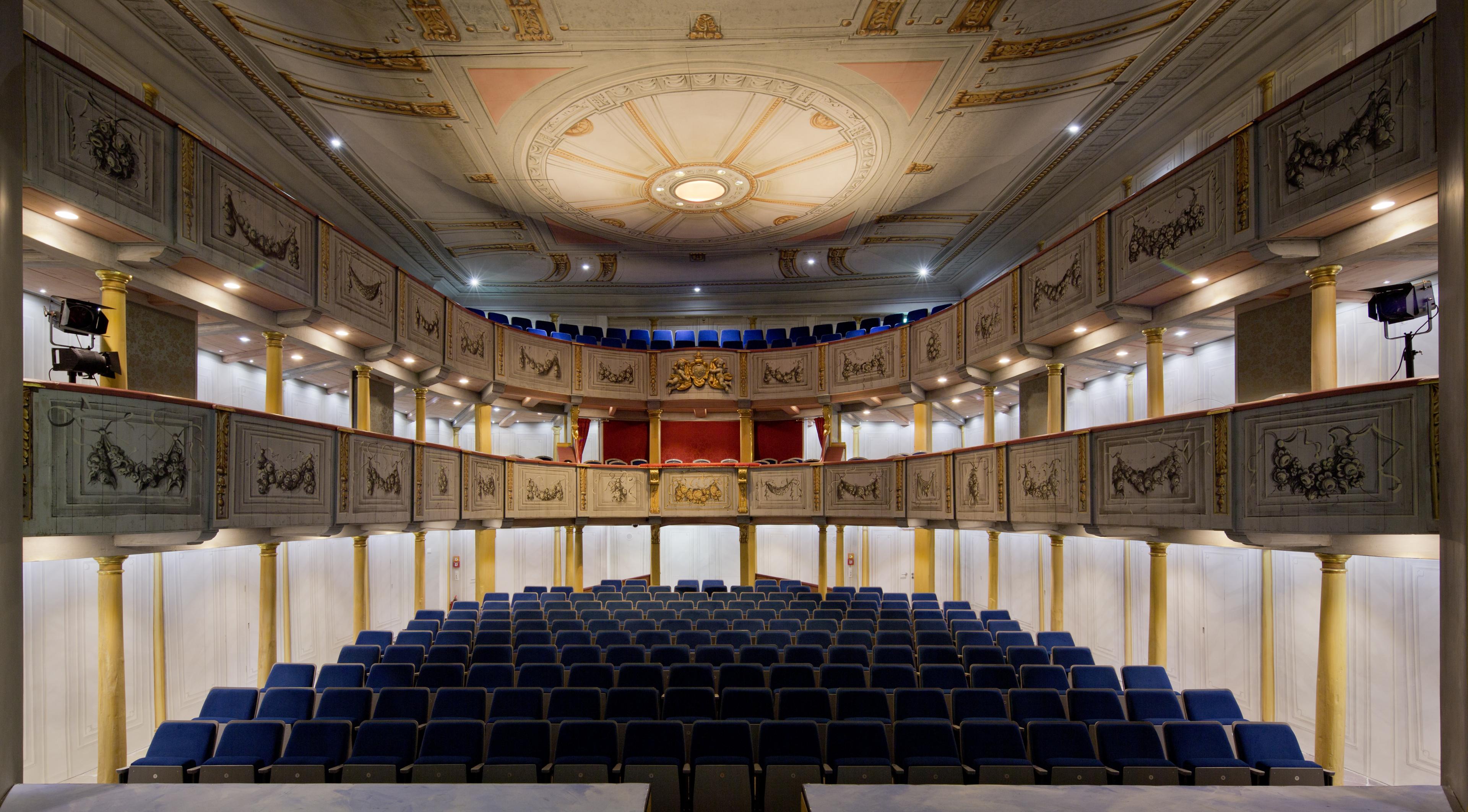 Blick in das Schlosstheater von der Bühne aus. Zu sehen sind die beiden ornamentverzierten Ränge und der untere Zuschauerraum mit seinen blau bespannten Sitzen.