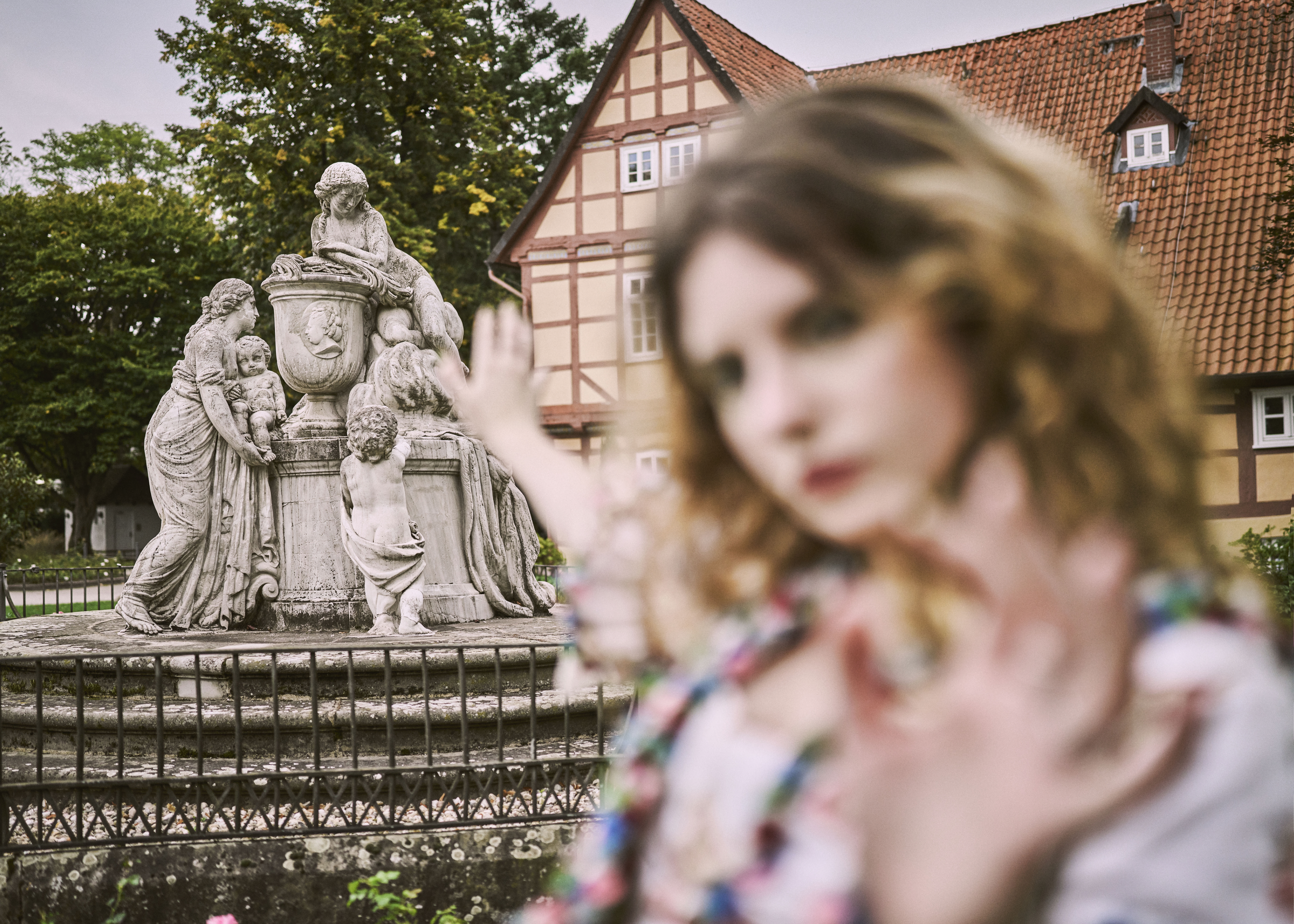 Eine Frau in historischem Kleid ist unscharf im Vordergrund vor dem Caroline Mathilde-Denkmal im Französischen Garten Celle zu sehen